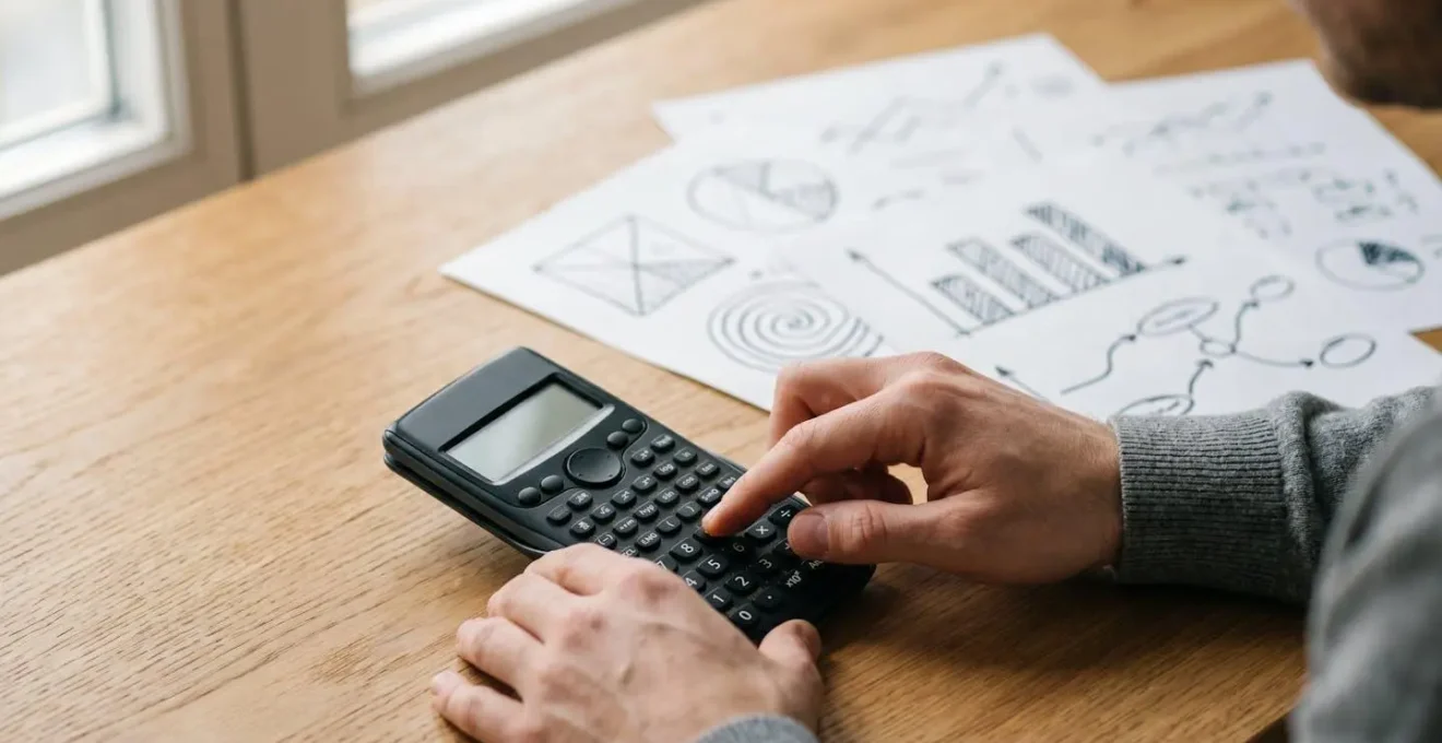 Gros plan sur des mains pianotant sur une calculatrice moderne avec des notes manuscrites financières en arrière-plan flou
